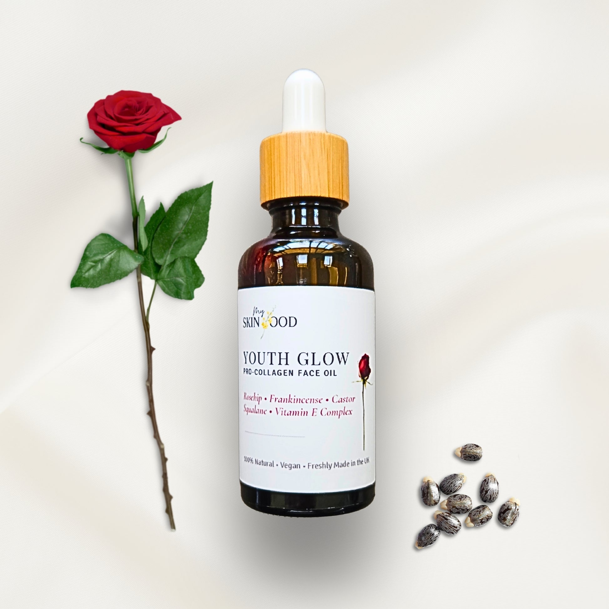 Bottle of My Skinfood 'Youth Glow' face oil with a red rose and seeds on a white background castor oil rosehip and frankincense serum 