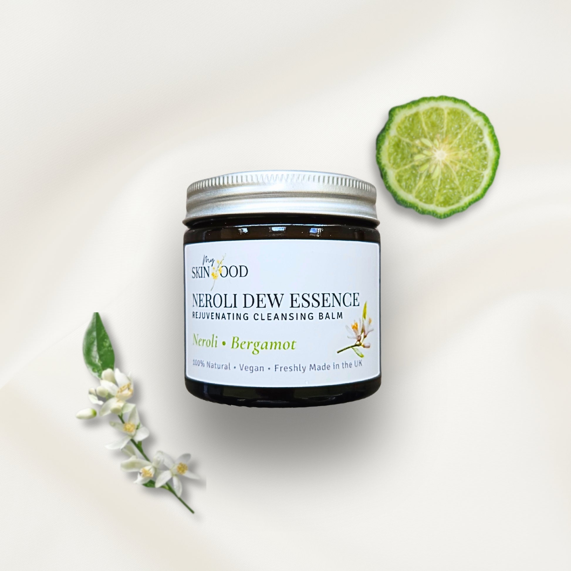 Jar of My Skinfood Neroli Dew Essence cleansing balm with a lime wedge and flowers on a light background