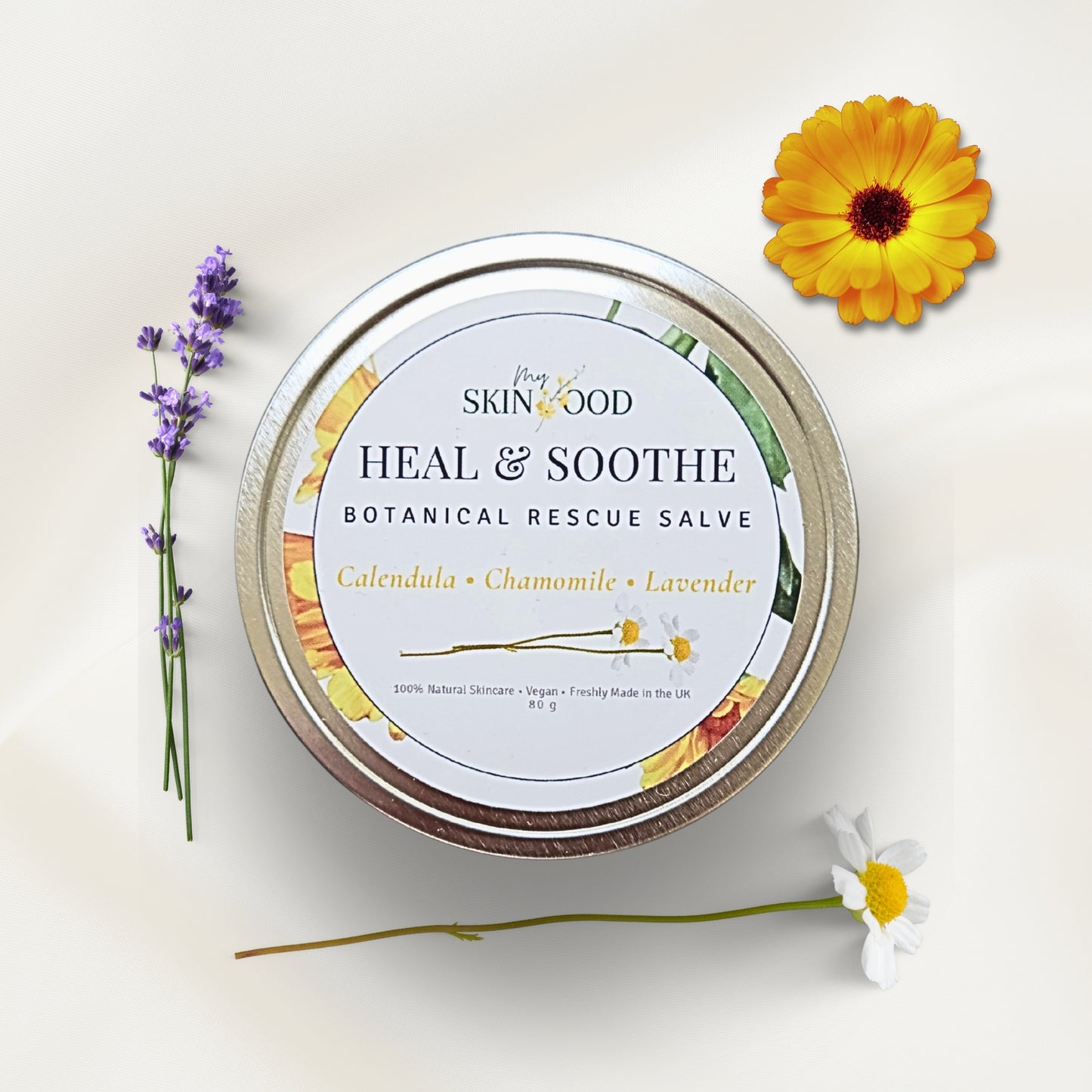 My Skinfood Heal & Soothe Natural Botanical Rescue Salve balm tin with Chamomile calandula and lavender flowers on a light background